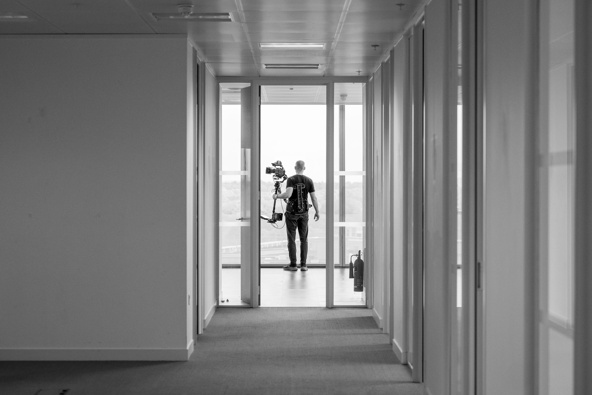 Long corridor in a modern office building with glass walls and natural light streaming in.