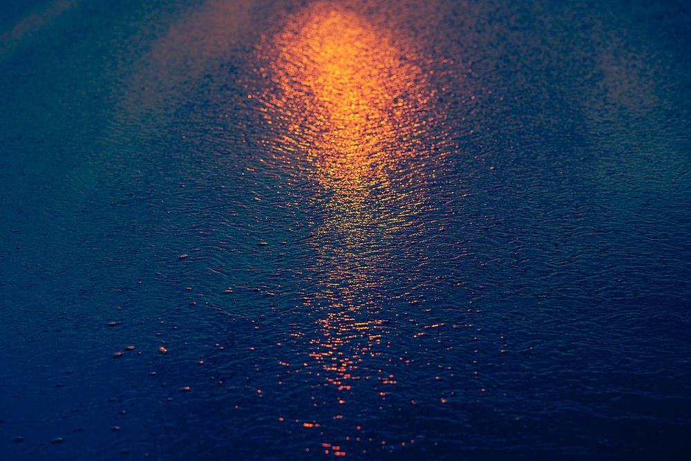 Golden sunlight reflection creates glowing path across dark blue rippling water surface.