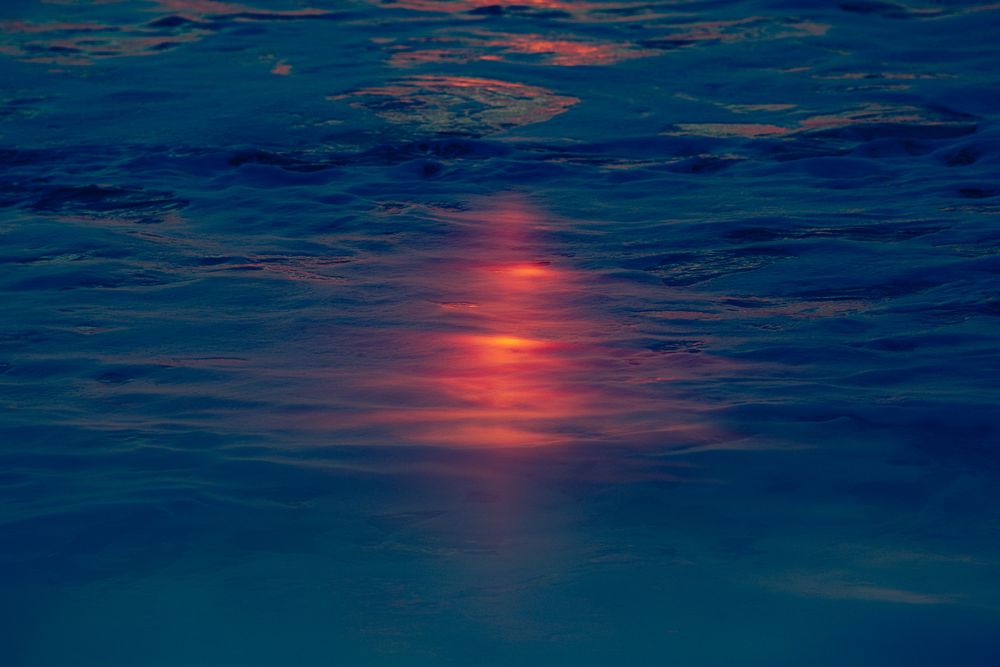Sunset reflection creates a glowing orange streak across dark rippling ocean waters.