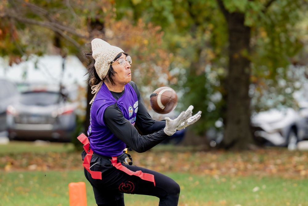 A flag football player in a purple jersey catches the football in a CMSA game