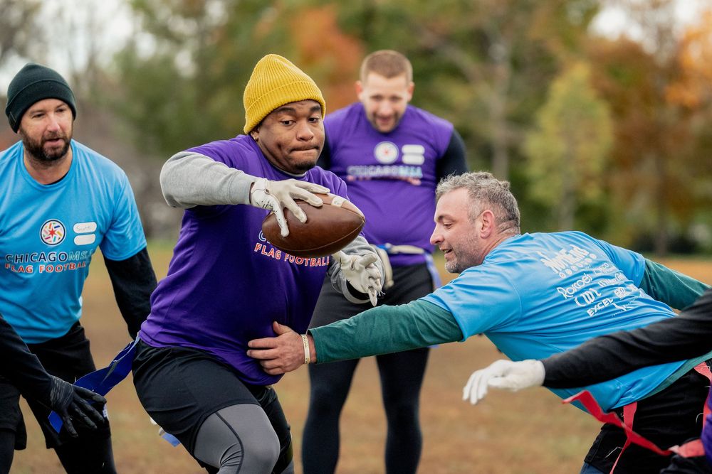 A flag football player in a purple jersey with the football dodges a flag pull from an opponent in a blue jersey in a CMSA game