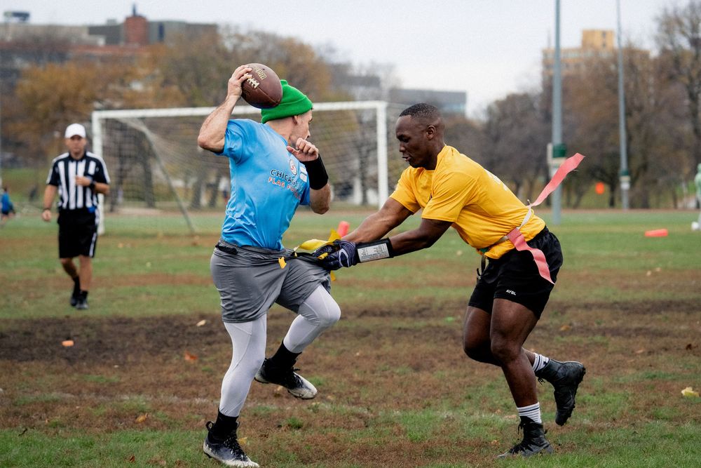 A flag football quarterback attempts to avoid getting their flag pulled by an opponent in a yellow jersey