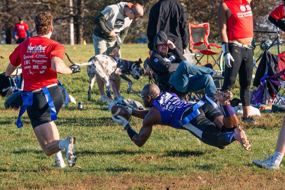 A flag football player in a purple jersey catches a football thrown low, fully outstretched and horizontal to the ground