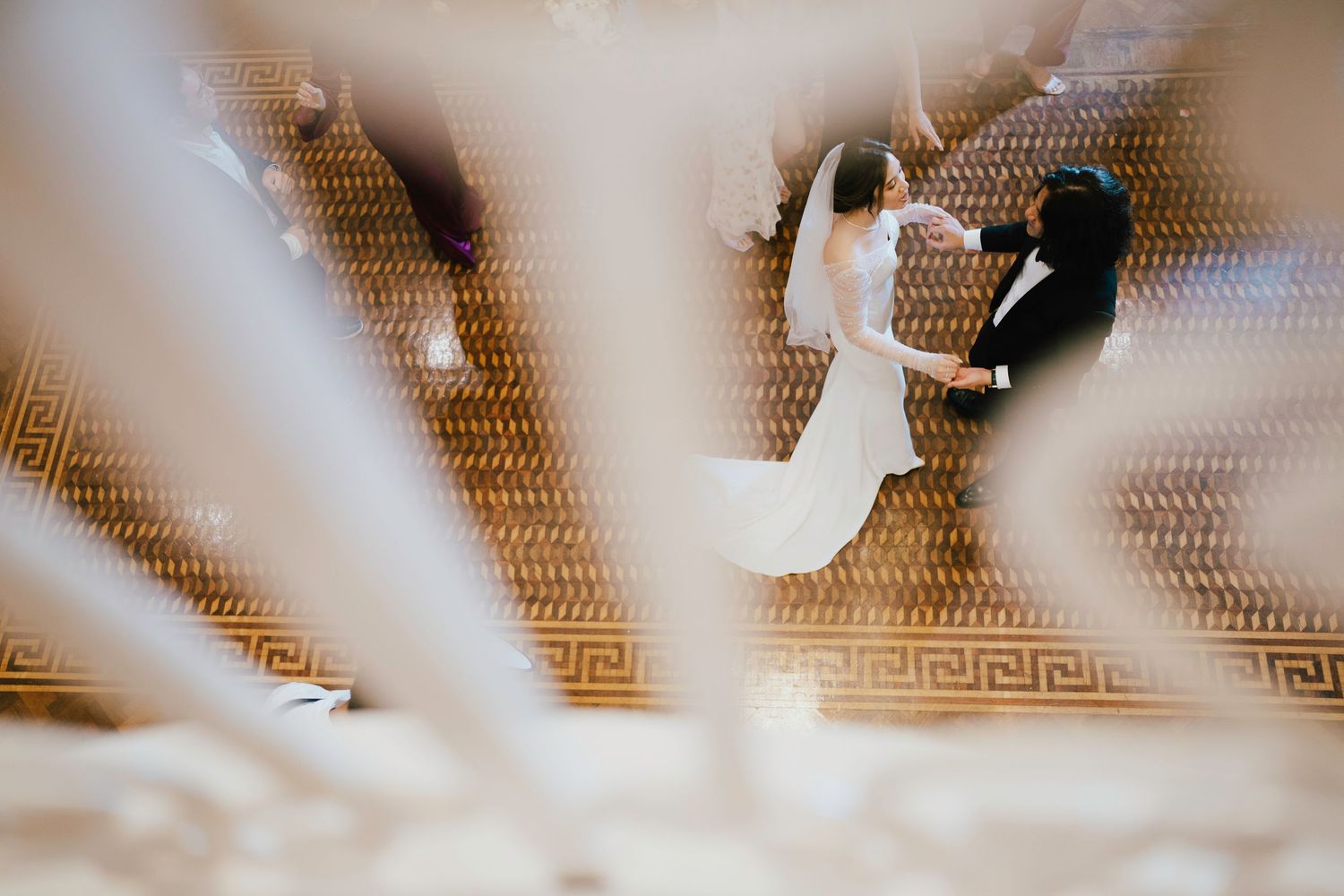 Bride and groom share first dance viewed from above on ornate patterned ballroom floor.