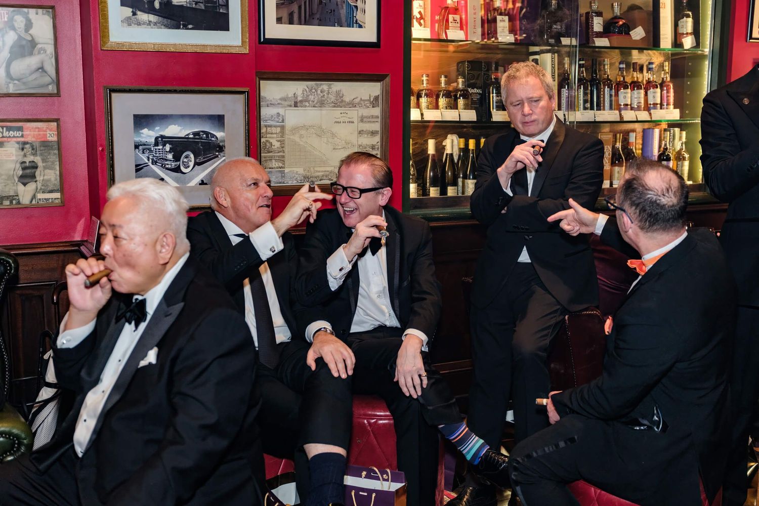 A group of people in formal attire sit at a bar and raise their glasses in a celebratory toast.