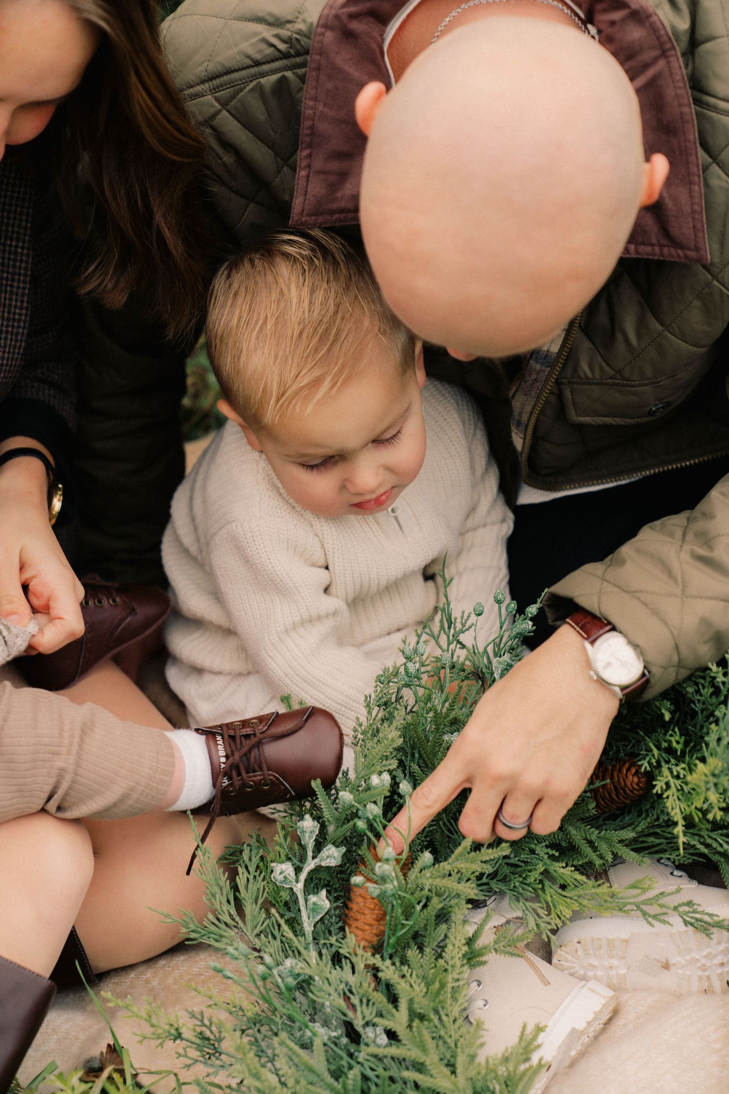 A toddler in a beige sweater explores green plants and foliage in a series of connected photos.