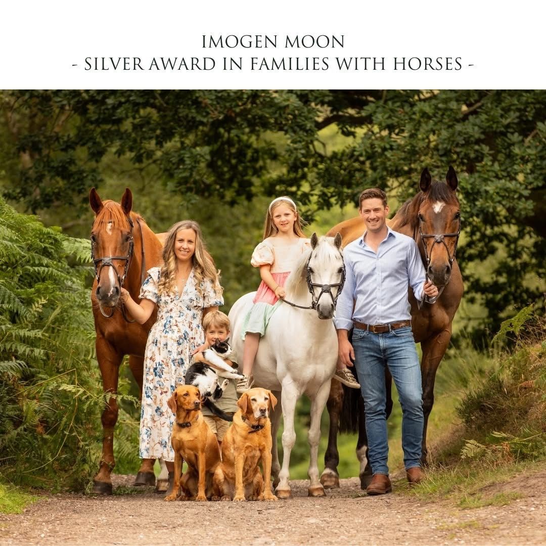 A group poses outdoors with horses, dogs and a pony on a wooded path surrounded by lush greenery.