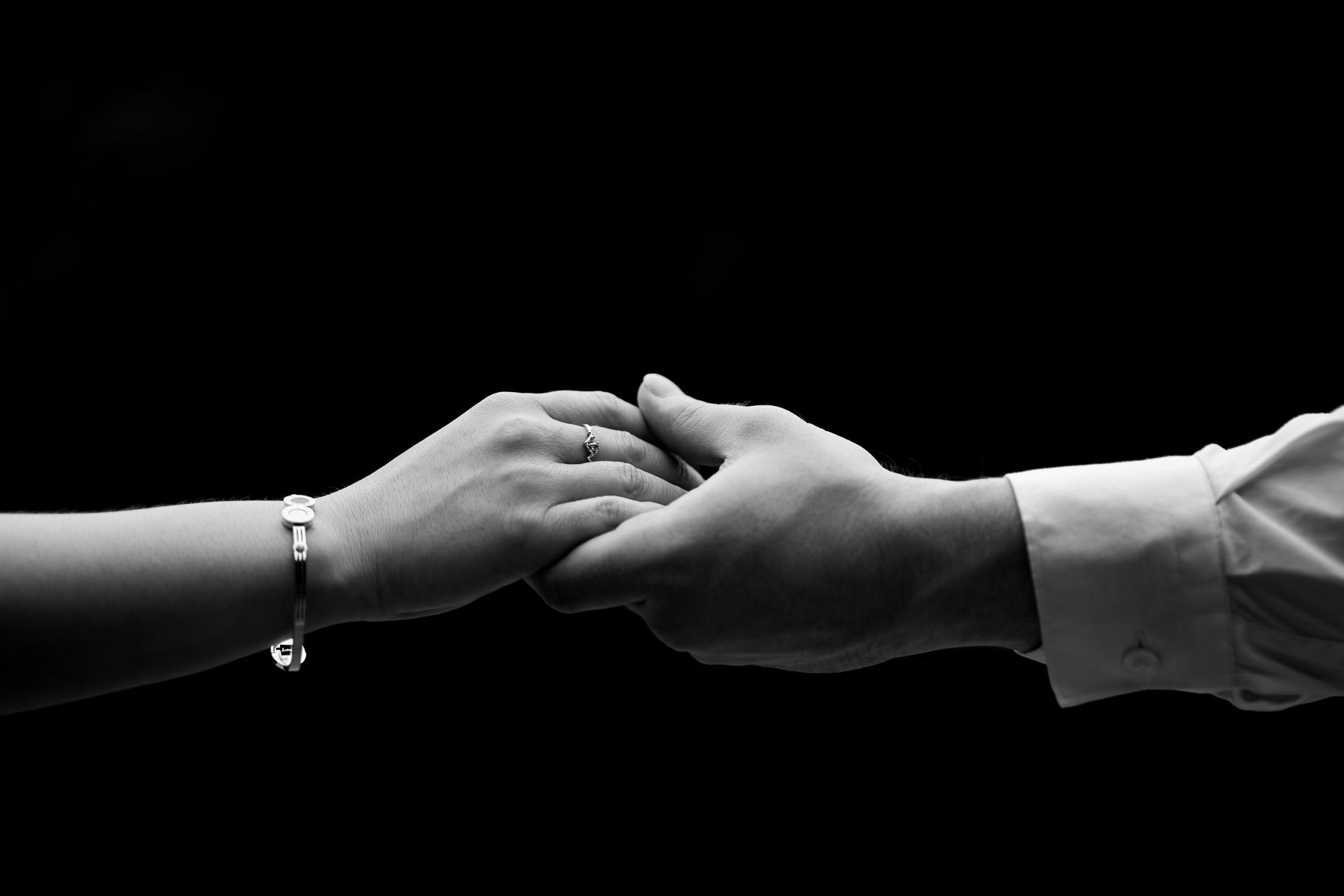 Black and white close-up of two hands reaching towards each other with jewelry visible.