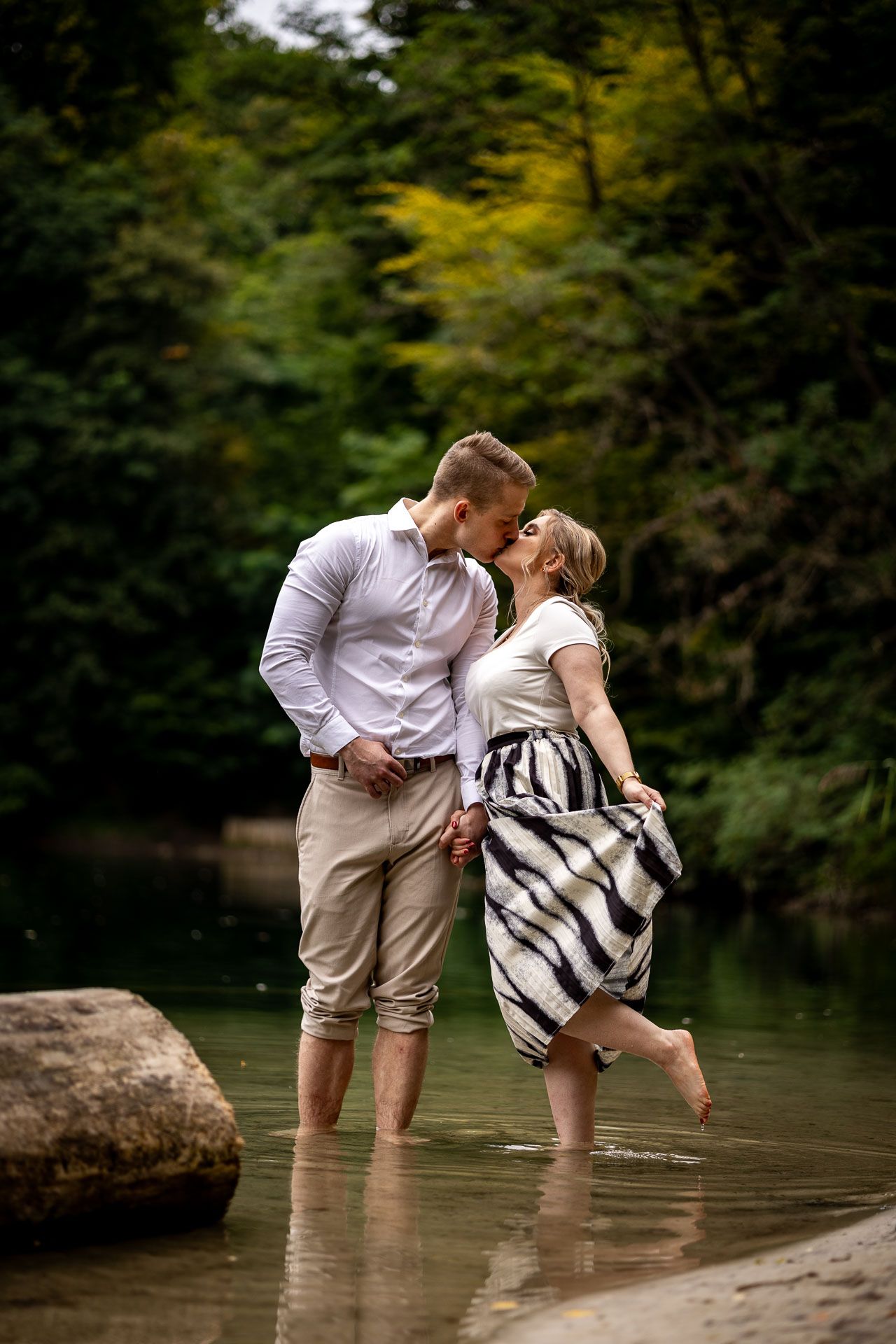 A couple shares a romantic moment while standing in shallow water near a lake.