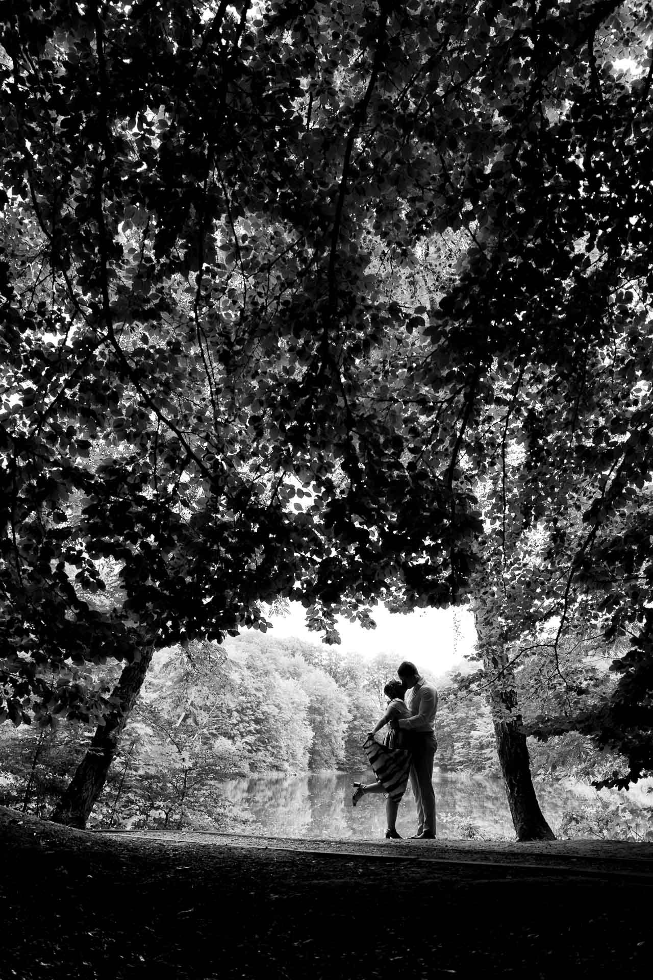 A silhouetted couple embraces against a backdrop of trees in black and white.