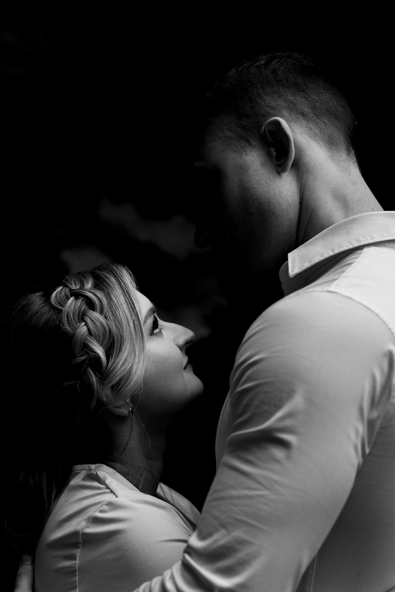 Black and white intimate portrait showing tender embrace in dramatic lighting.