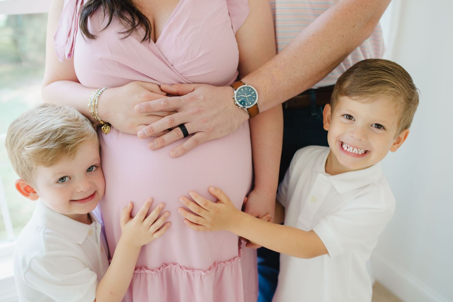 A family wearing pink and white outfits sits together on a white couch for a casual portrait session.