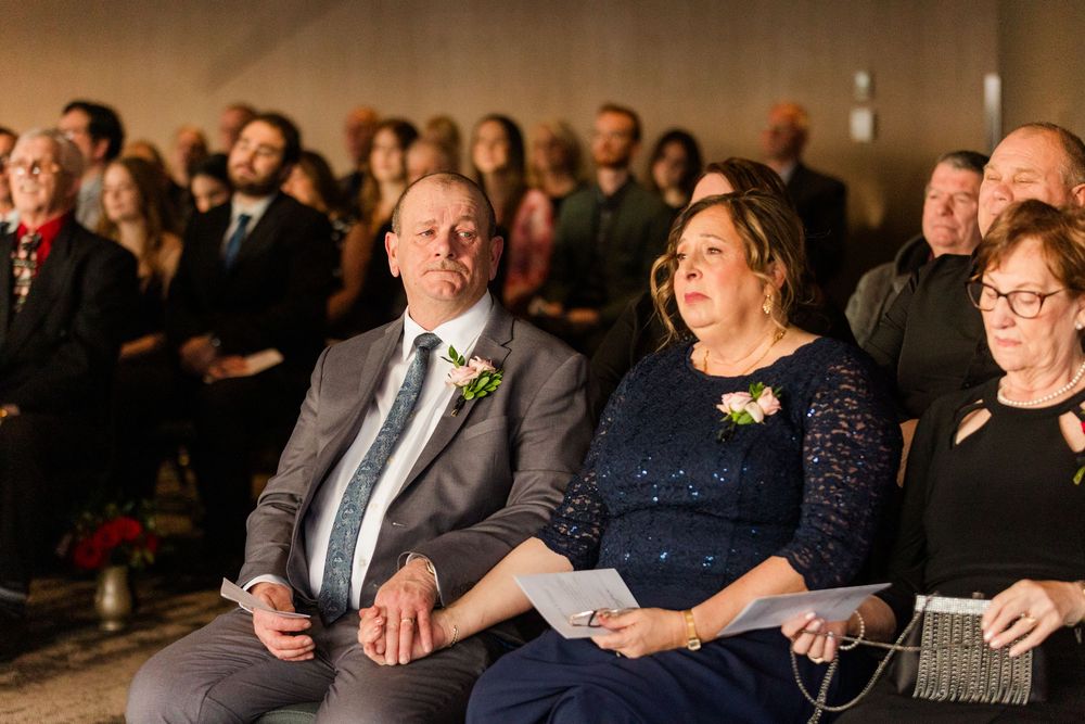 Wedding guests seated in rows watching an emotional ceremony in a dimly lit venue.