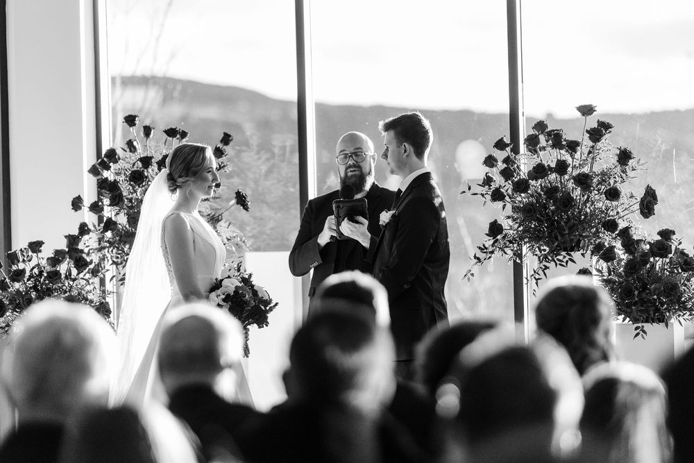 Wedding guests seated in rows watching a ceremony against a bright window backdrop.