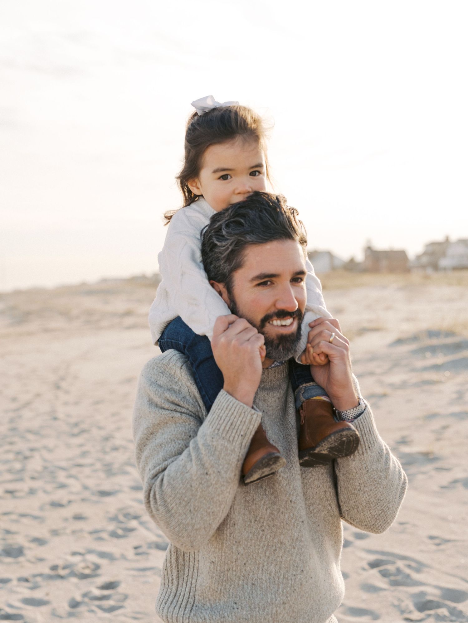 Father embracing his daughter as she sits on his shoulders with ocean views during a fall beach session in Monmouth County.