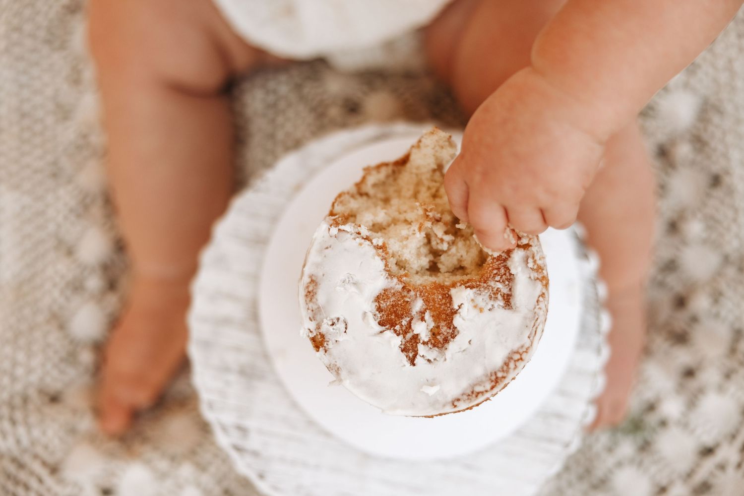 Small hands reach for a chocolate-filled powdered donut on a white plate against a speckled gray surface.