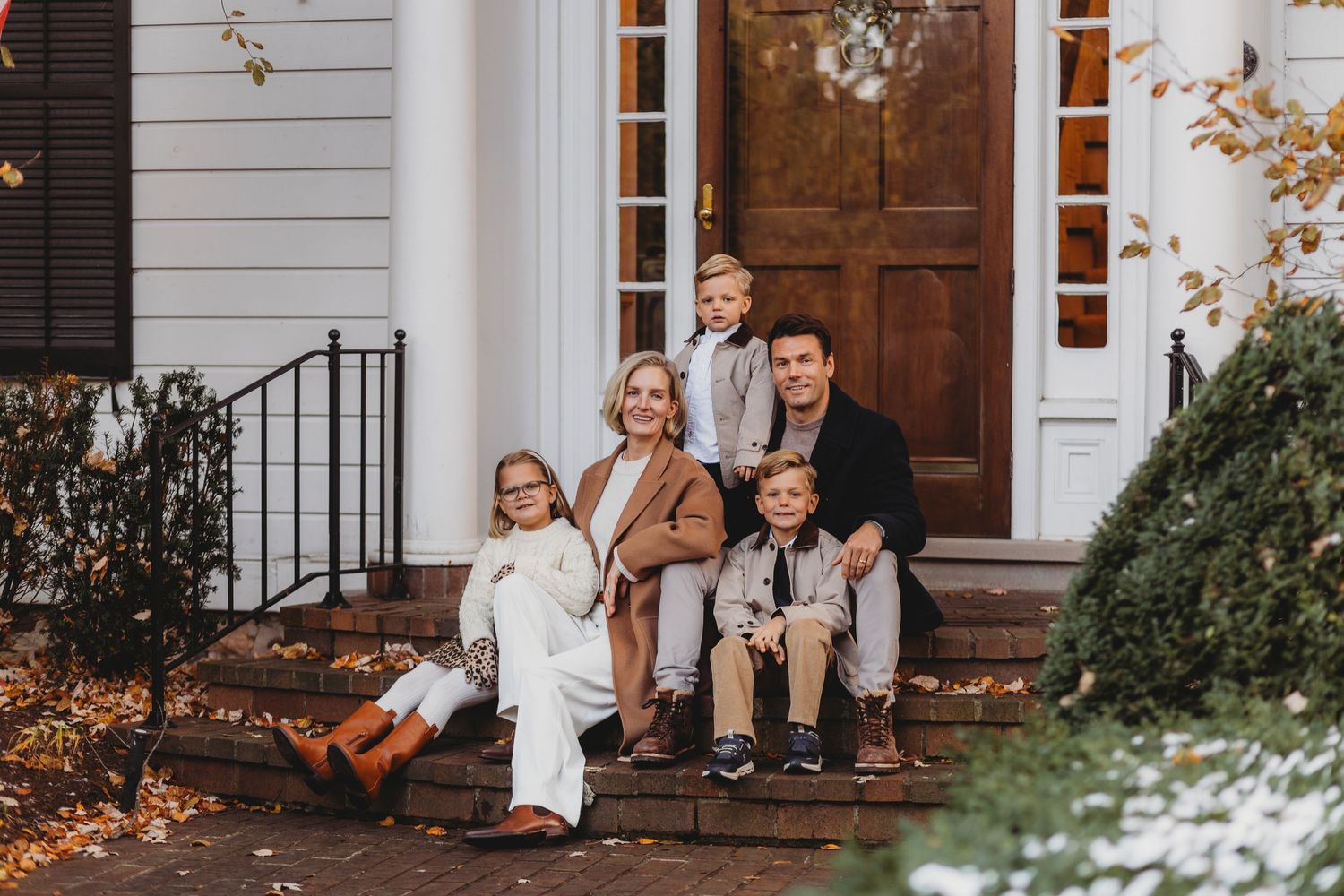 A group sits on a white porch with autumn decorations and pumpkins during a fall photo session.