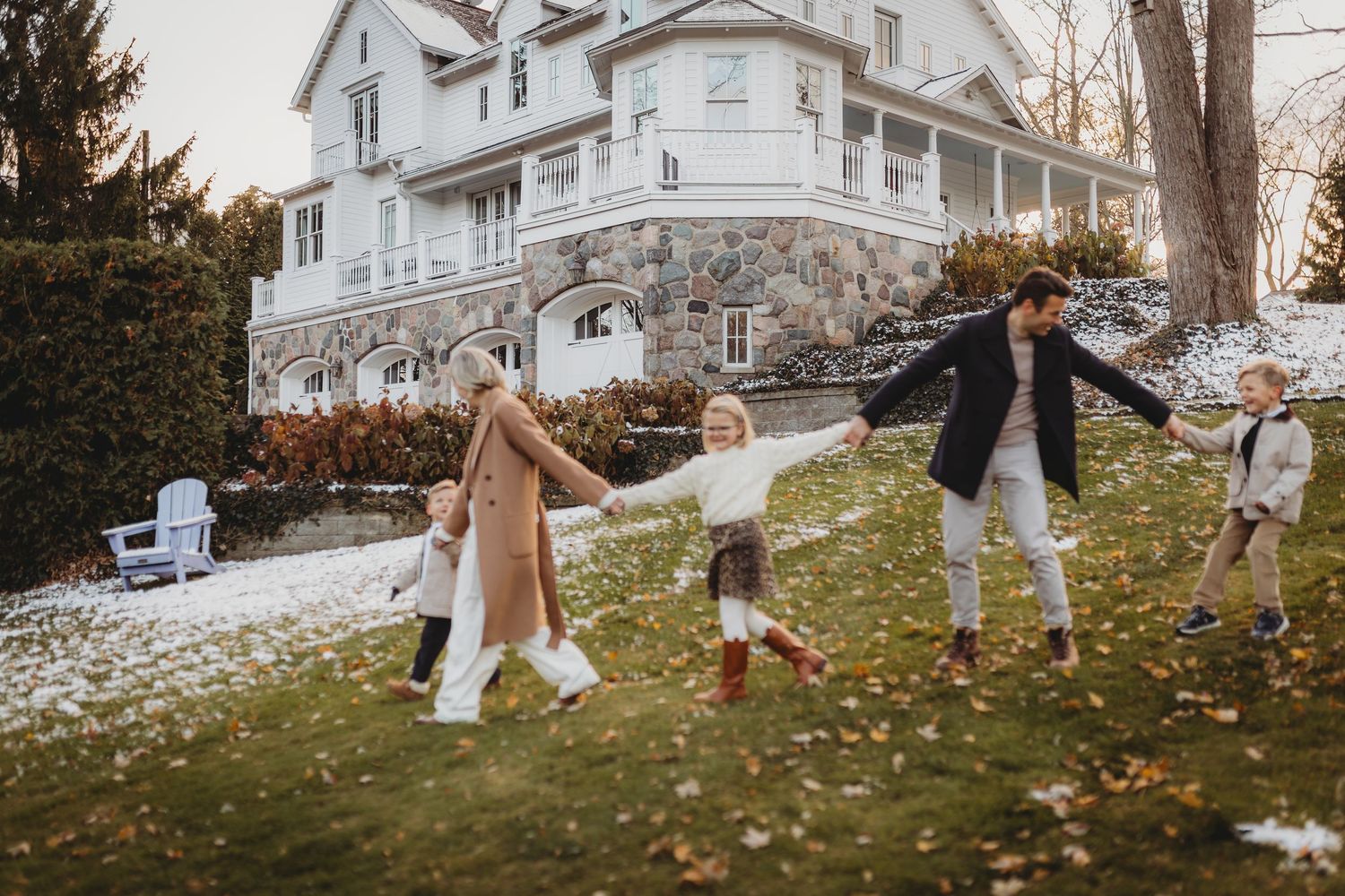 Family having fun playing and throwing autumn leaves on a grassy hill near a white house.