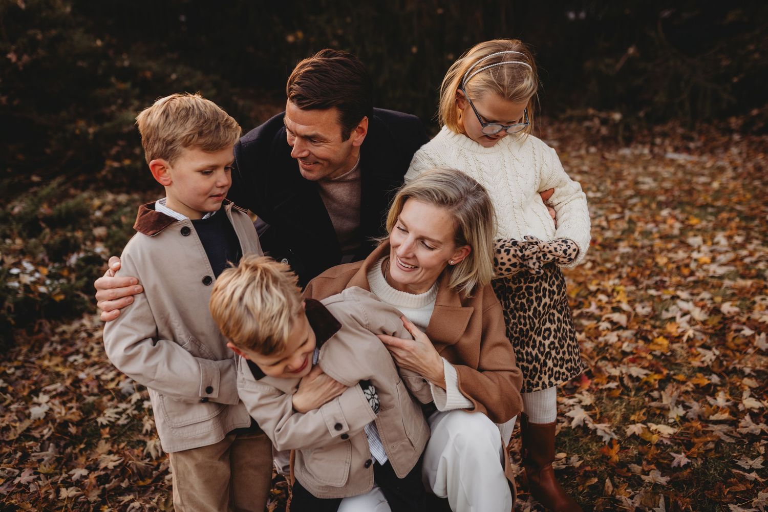 A family shares joyful moments together while sitting in autumn leaves during an outdoor photo session.