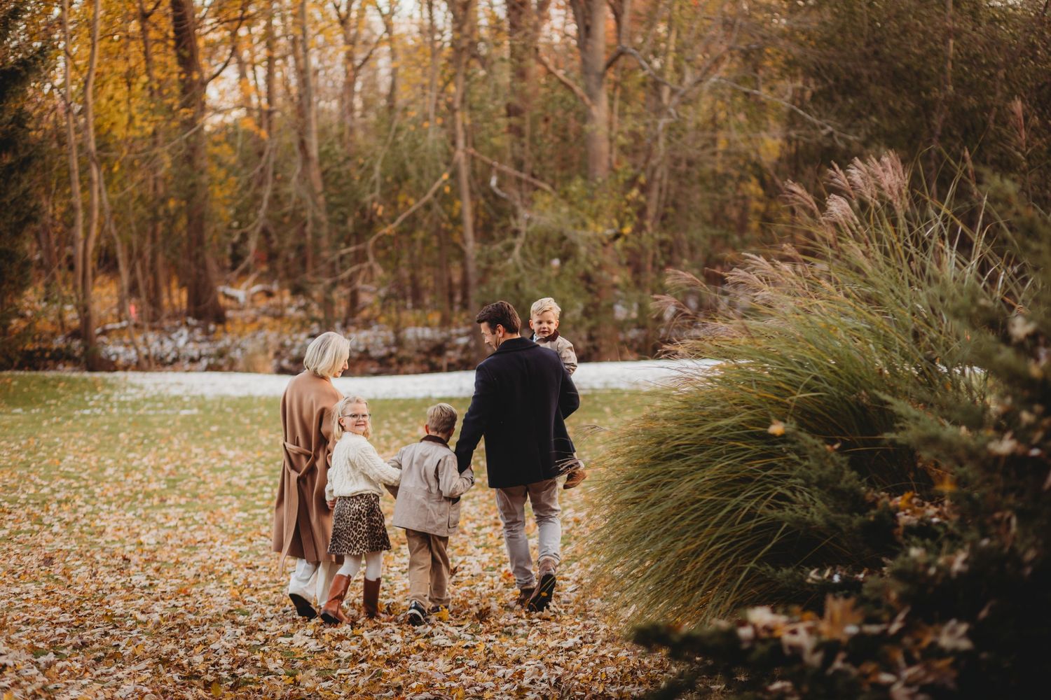 A family walks together through a scenic autumn forest with golden leaves and warm sunlight filtering through trees.