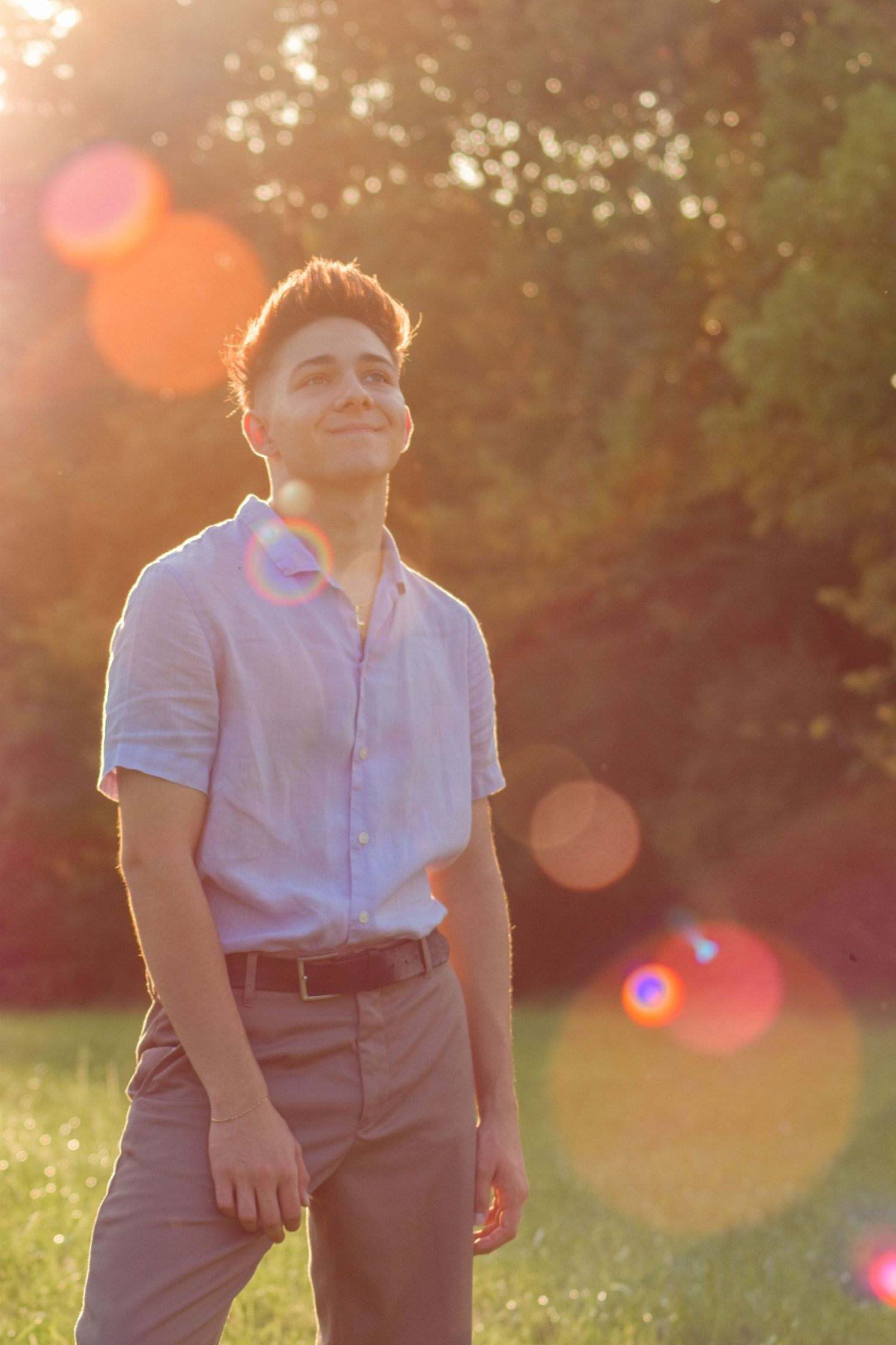 Portrait of someone in casual attire smiling during golden hour with lens flares.