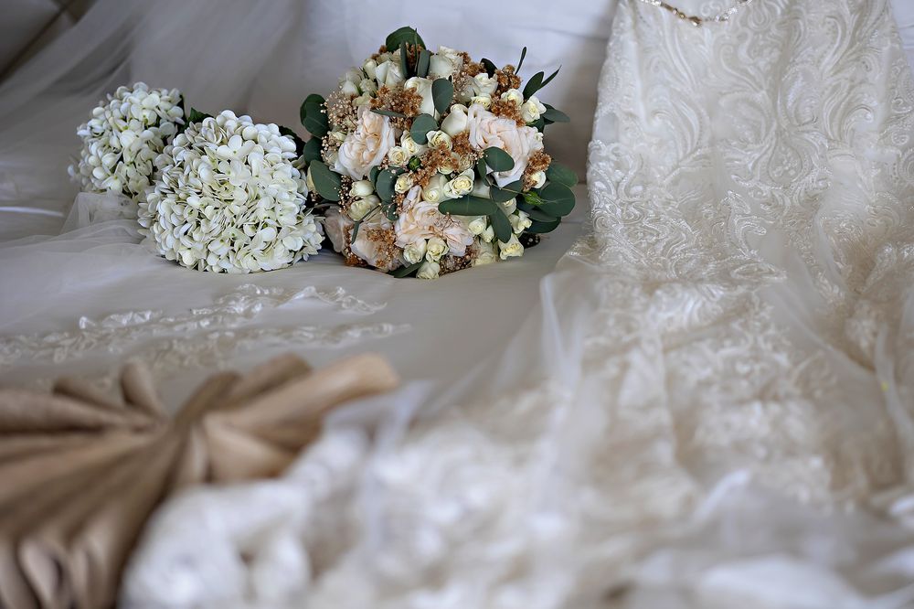 Elegant white and peach floral wedding bouquet rests on soft beige fabric with delicate lace details.