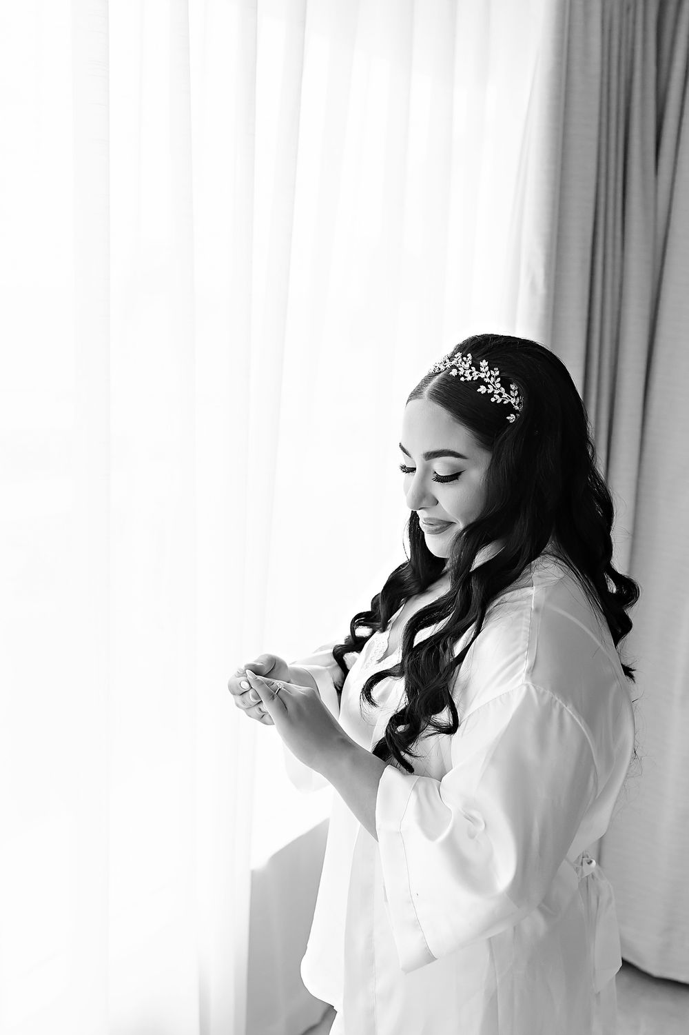 Black and white series showing a bride getting ready in a white robe against a bright window backdrop.