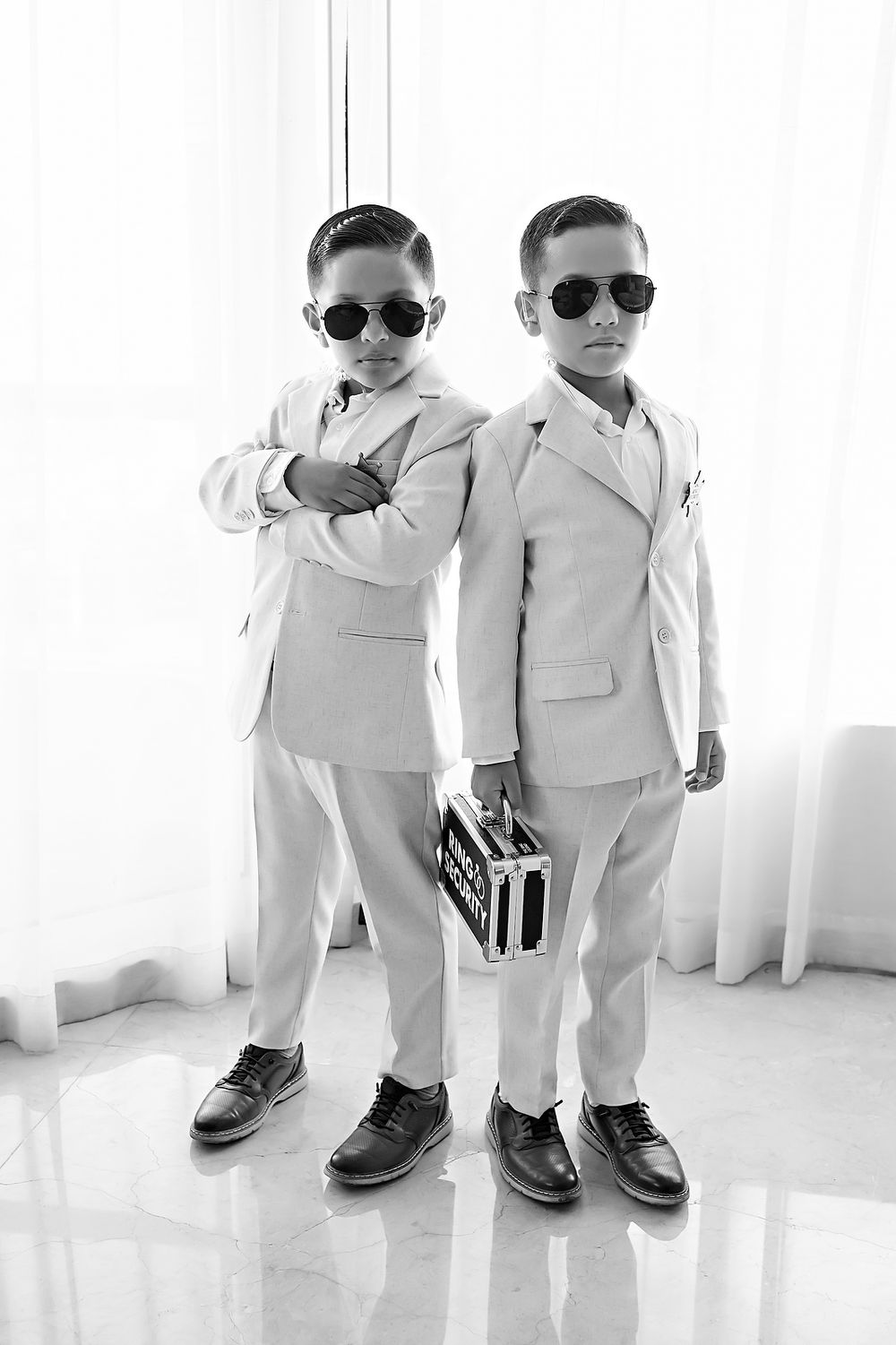 Young ring bearers in matching white suits and sunglasses pose for wedding photos.