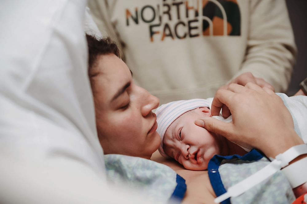 A close-up view of a mother gently kissing her newborn baby while lying together in a white bed.