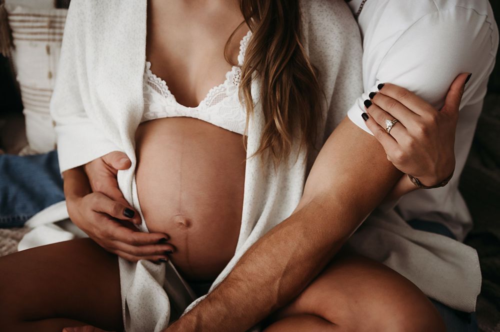 Intimate maternity photo showing hands cradling a pregnant belly while wearing a white button down shirt.