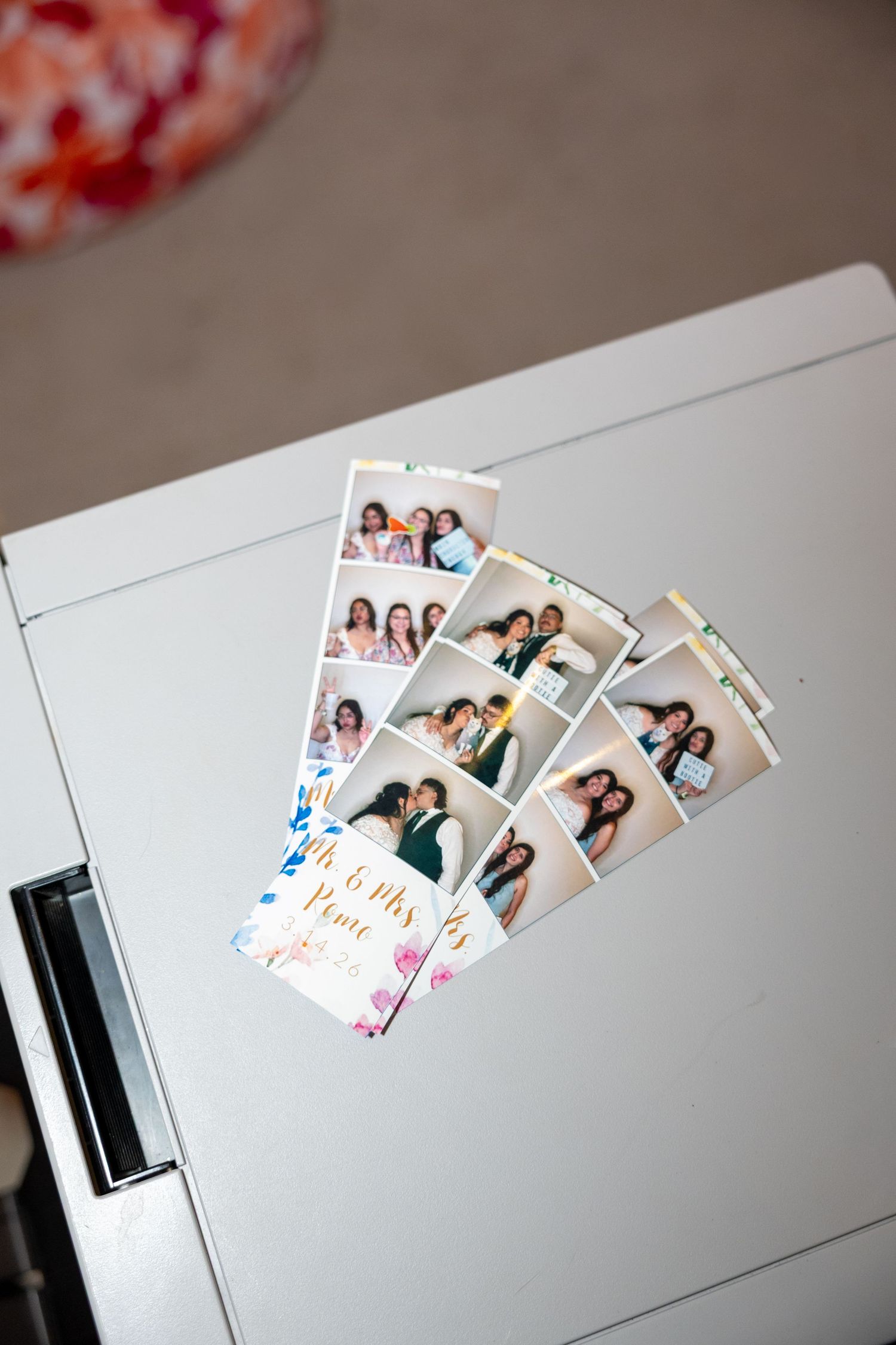 Wedding photo booth strips featuring couples and guests displayed on a printer.