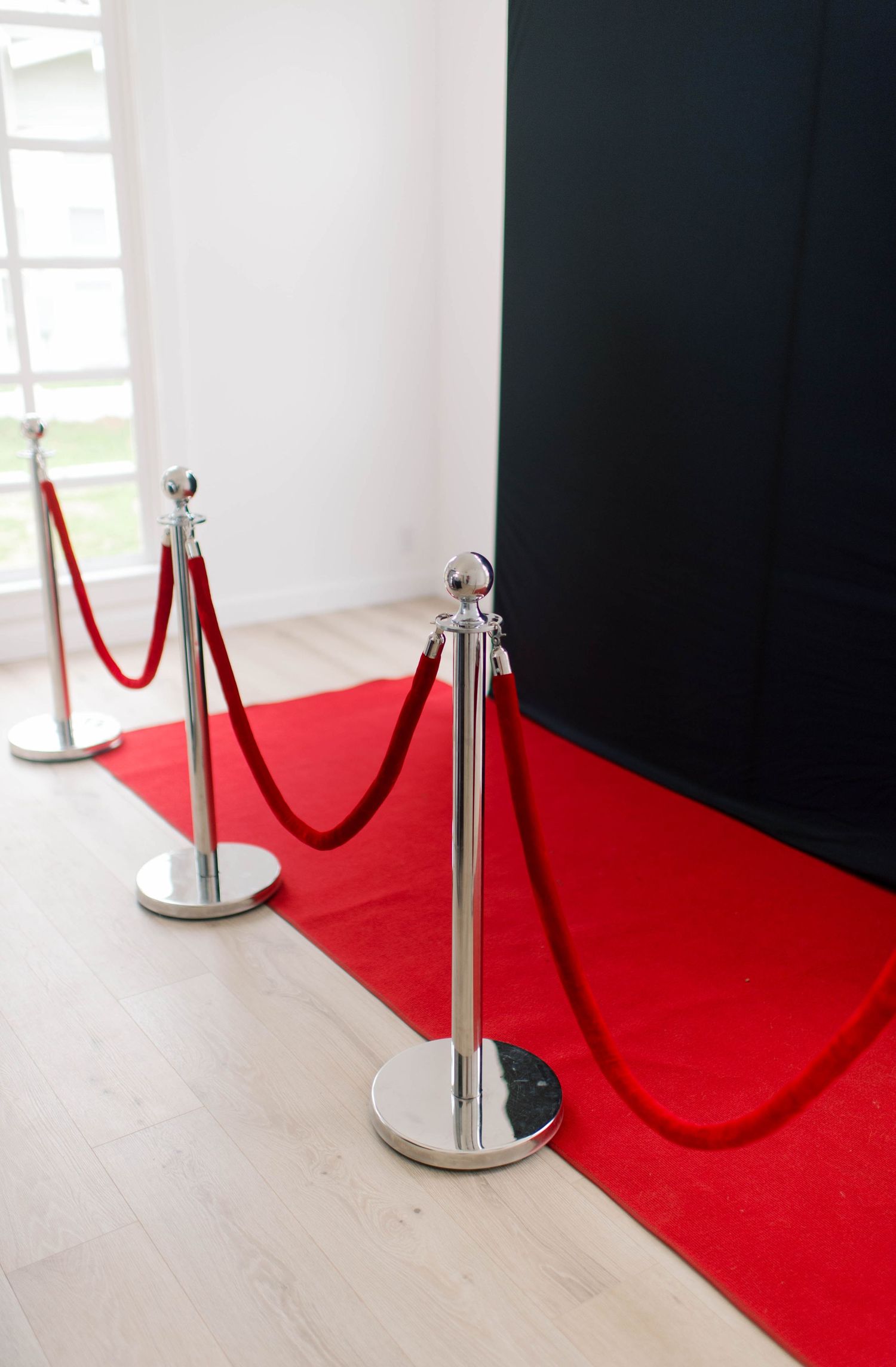 Red carpet entrance with silver stanchions and velvet ropes in front of a black backdrop.