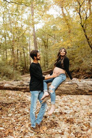 A couple shares a tender moment in an autumn forest setting with fallen leaves and a rustic log.