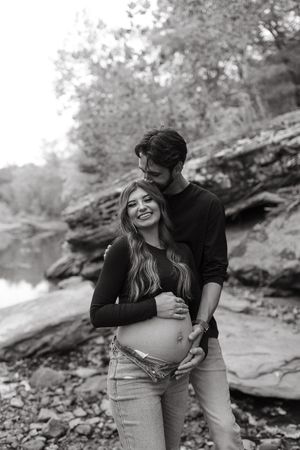 A couple shares an intimate black and white maternity photoshoot moment outdoors against a rocky natural backdrop.
