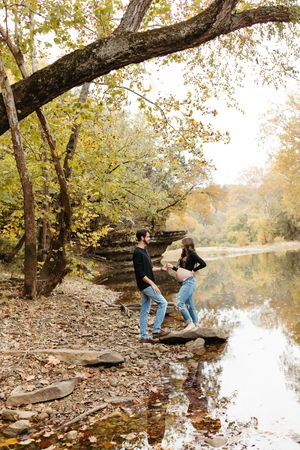 A sequence of people exploring a serene autumn riverbank with fallen leaves and reflective water.