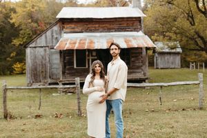 A couple shares romantic moments in a rustic outdoor setting with fall foliage and wooden barns in the background.