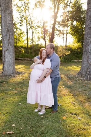 A loving family moment captured in a sunlit wooded area during golden hour as sunlight filters through the trees.