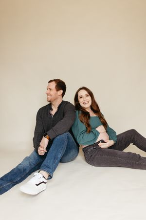 A couple lounges casually on a cream-colored backdrop during an indoor photo session.