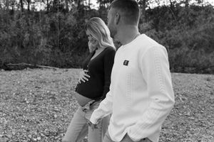 A couple in white clothing embraces while walking through a scenic outdoor setting in black and white photography.