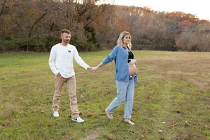 Couple walking hand in hand through a grassy meadow during a golden hour outdoor photo session.
