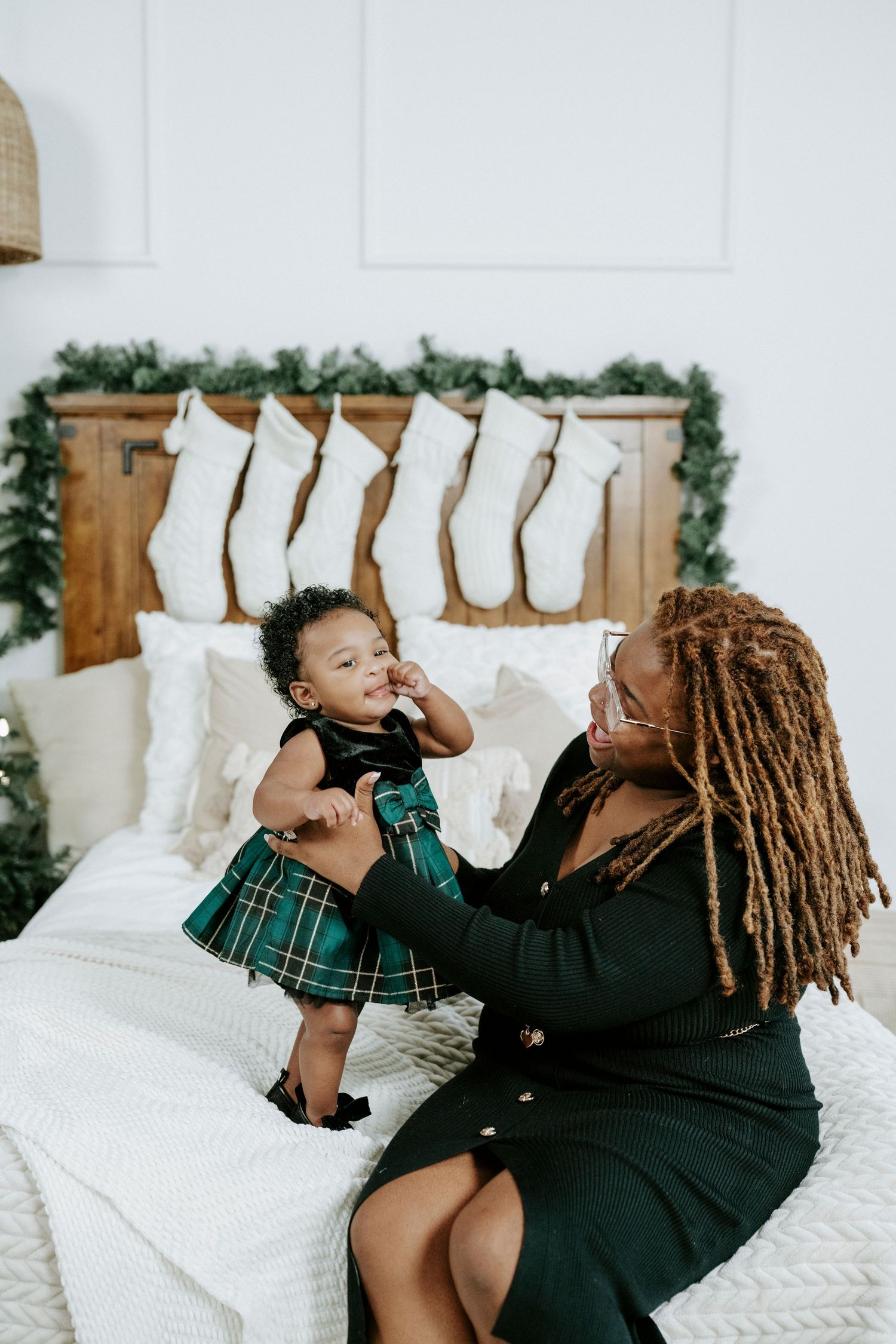A holiday scene with white stockings hanging on wood panel and two people sitting on a white bed sharing a joyful moment.