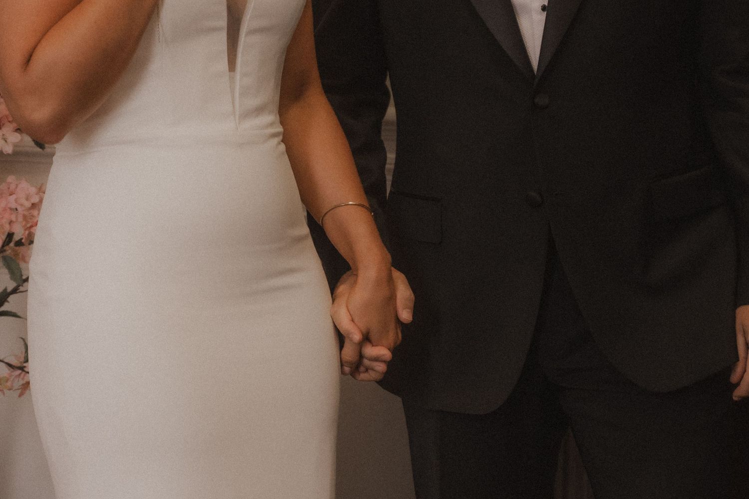 Wedding party members pose in formal attire while standing in line against a neutral background.