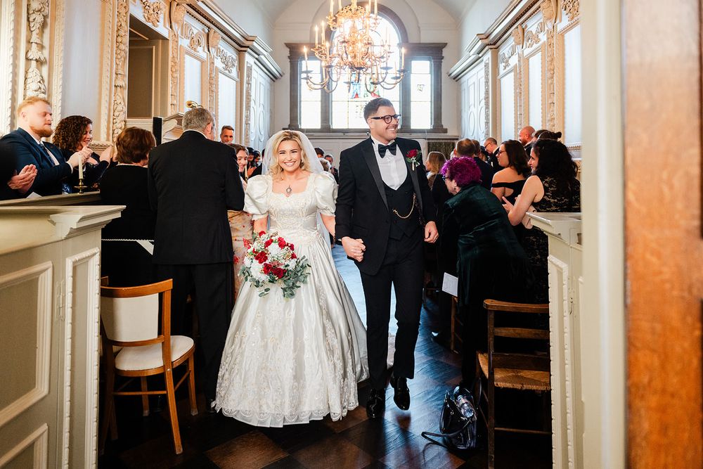 Wedding party walks down an elegant hallway with ornate chandeliers and marble columns in a luxury venue.