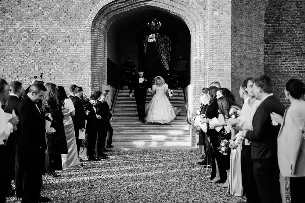 Wedding guests line up outside a stone church entrance to throw rice at the newlywed couple.