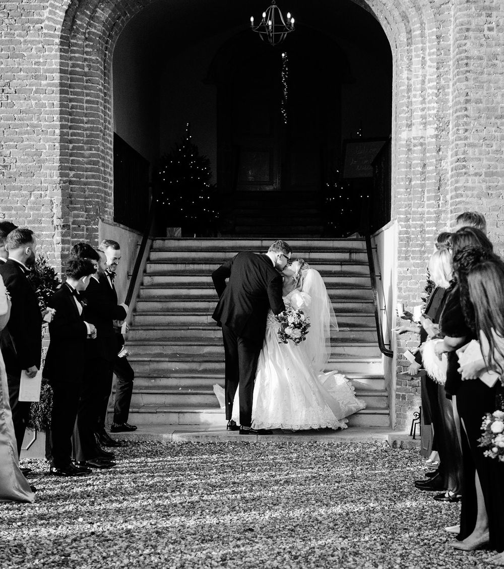 A black and white wedding photograph showing a couple ascending church steps while guests line the sides.