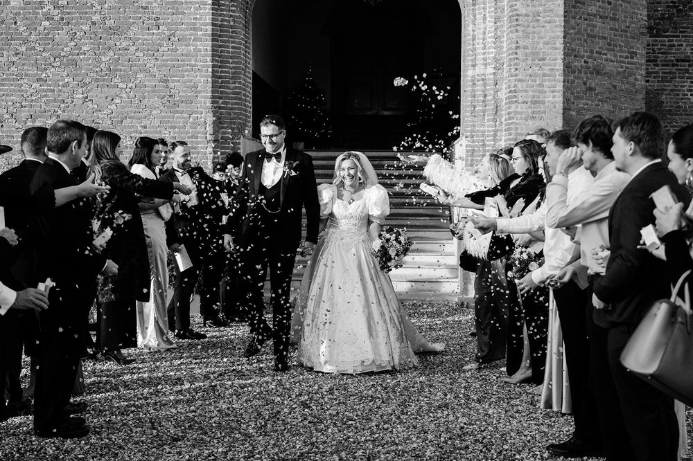 Wedding guests celebrate by tossing white flower petals as newlyweds exit a traditional church ceremony.
