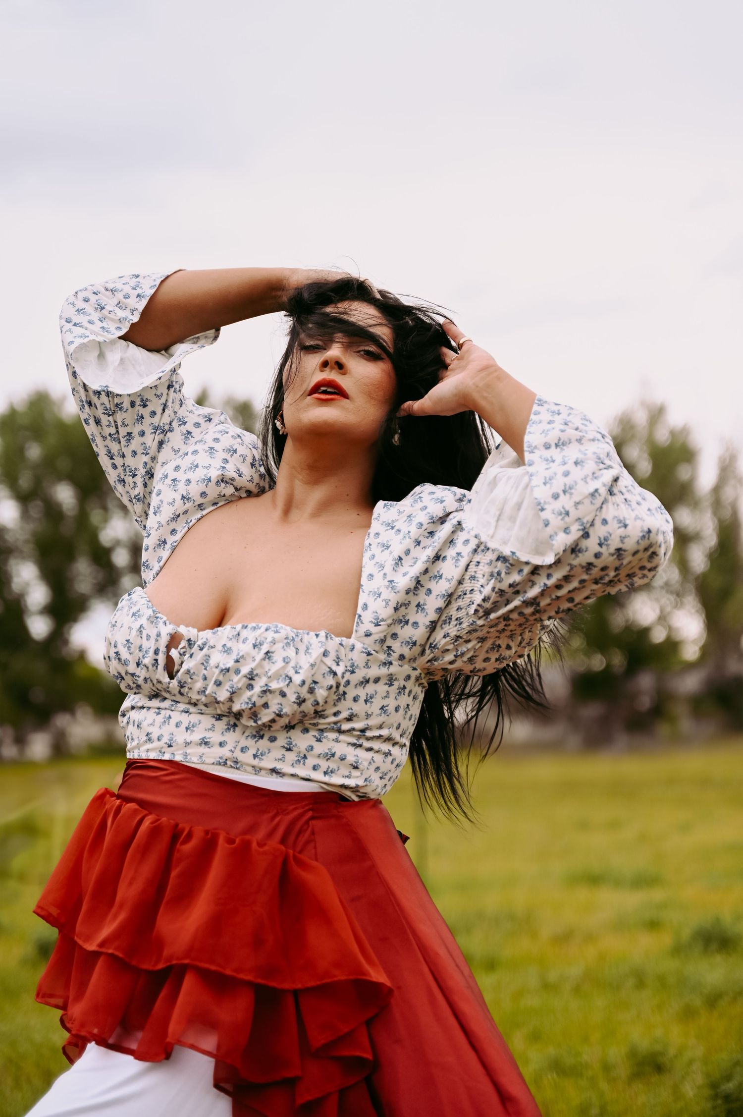 A posed outdoor fashion photo featuring a white floral puff sleeve crop top paired with a dramatic red ruffled skirt.