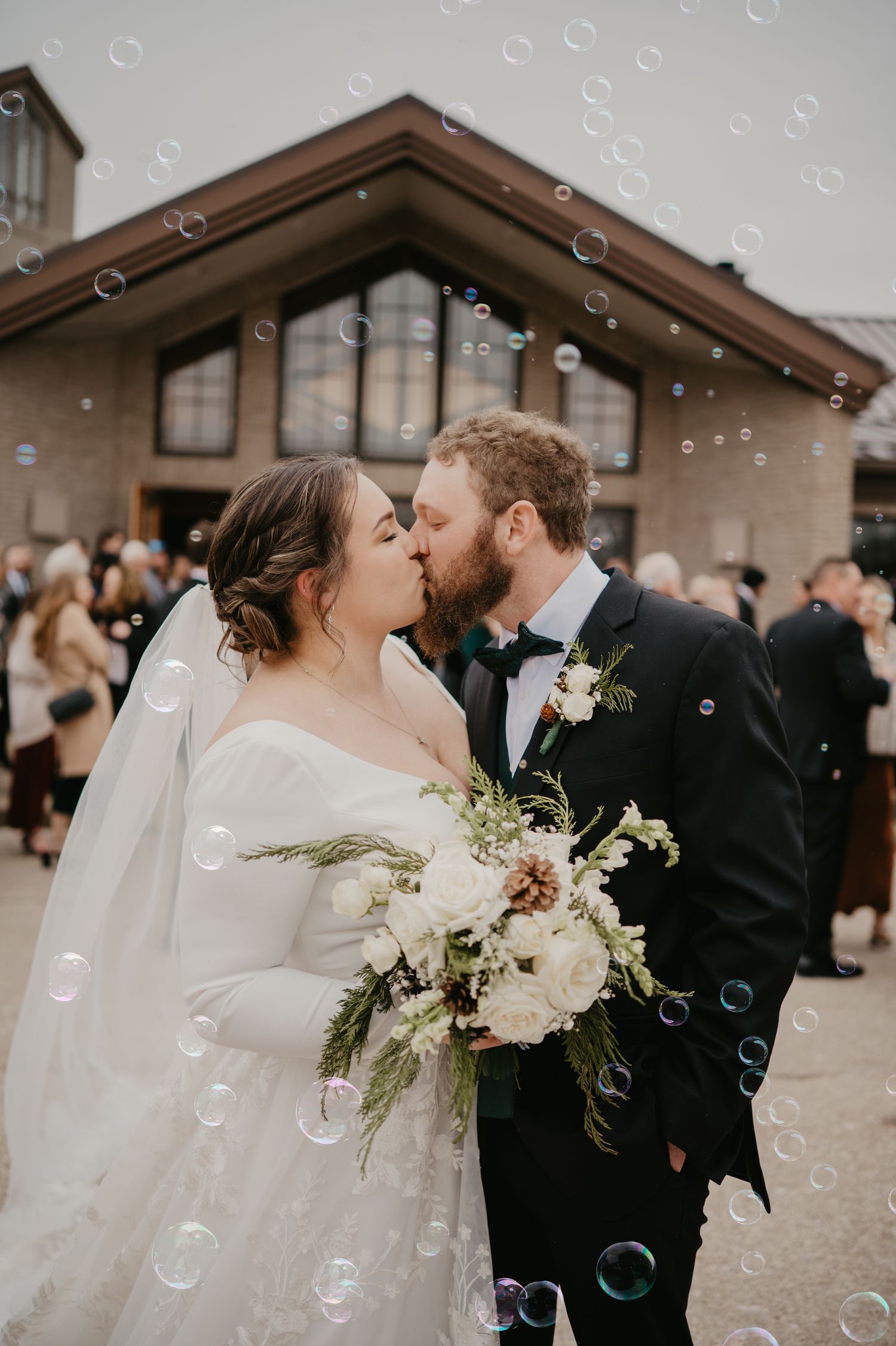 Newlyweds share a kiss surrounded by bubbles outside a church after their wedding ceremony.