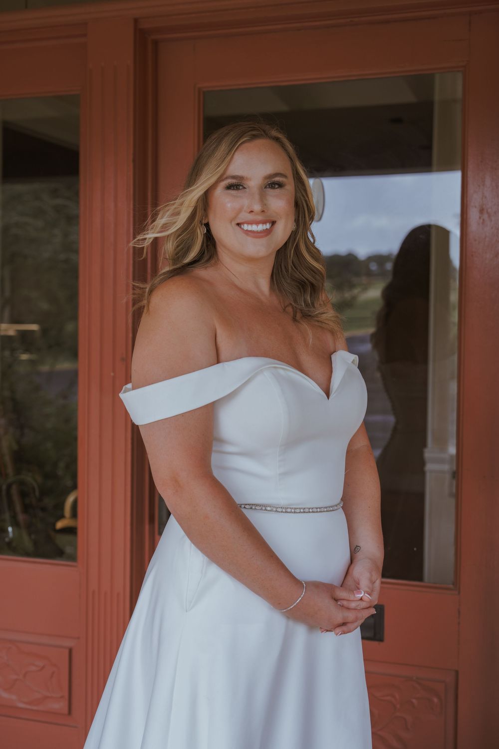 Elegant white wedding dress with asymmetrical neckline photographed against rustic red doors.