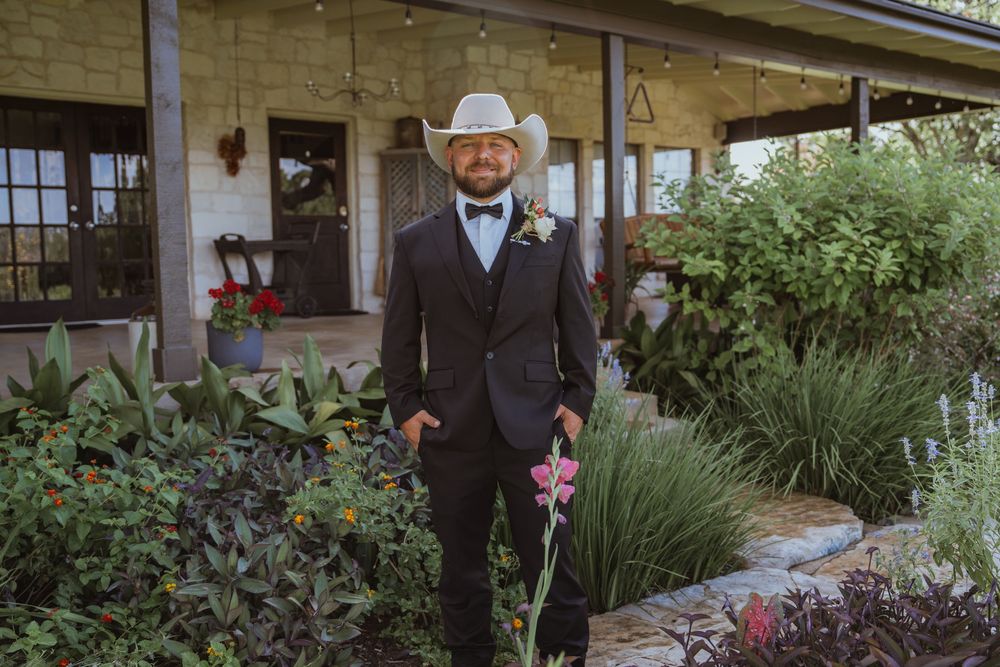 Wedding party members in formal attire posed along garden pathway with flowering plants.